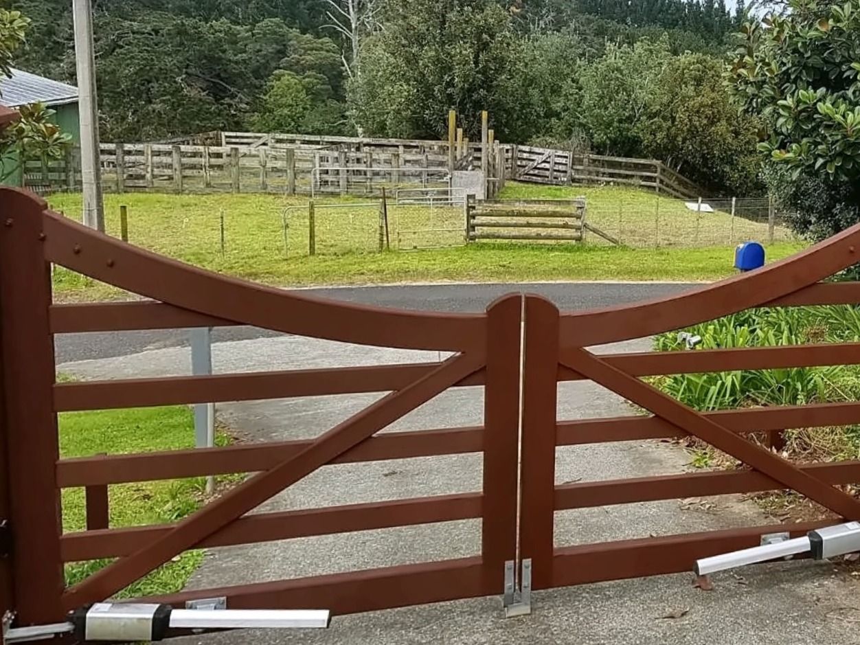Timber driveway gates restored and stained a deep red-brown, closed across a concrete driveway.