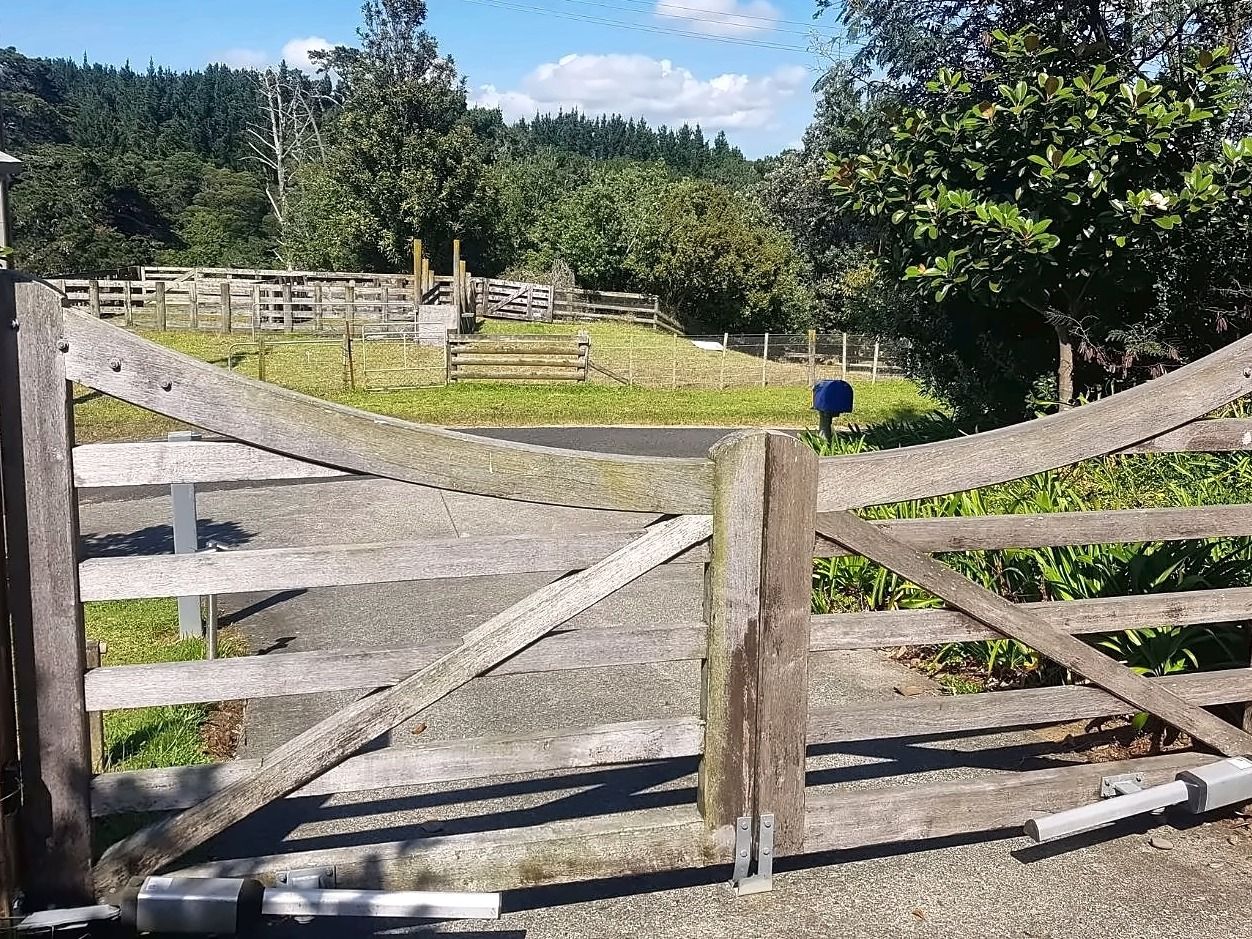 Weathered grey timber driveway gates, a pair with curved top rails and diagonal braces, before restoration.