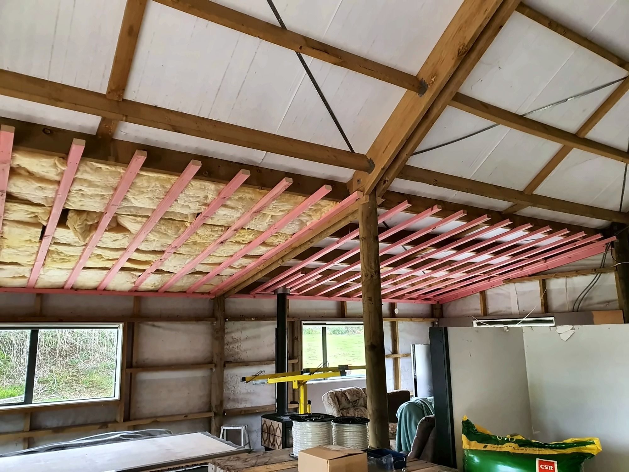 Pink timber ceiling battens fixed under the roof framing, with yellow insulation batts going in above them.