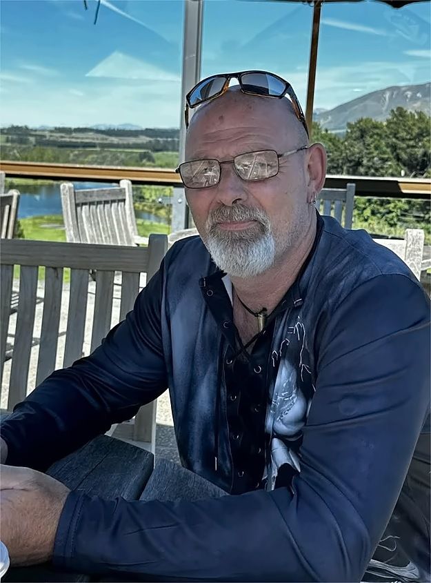 Mike Powell, owner of Powell's Property Maintenance, sitting at an outdoor table with hills behind him